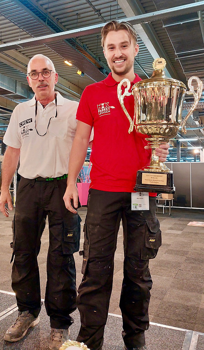 Mika Stevens, de nieuwe Nederlands Kampioen Parketleggen, ontvangt uit handen van Jan van der Kroef de gelijknamige bokaal.