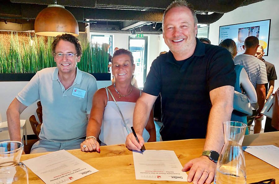 Mano Demmers zoals altijd geflankeerd door partner Cindy tekent voor de Gerflor display Dick van de Klok kijkt namens Flamingo tevreden toe